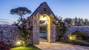 Um arco de pedra com um portão, rodeado por plantas floridas e um muro de pedra.