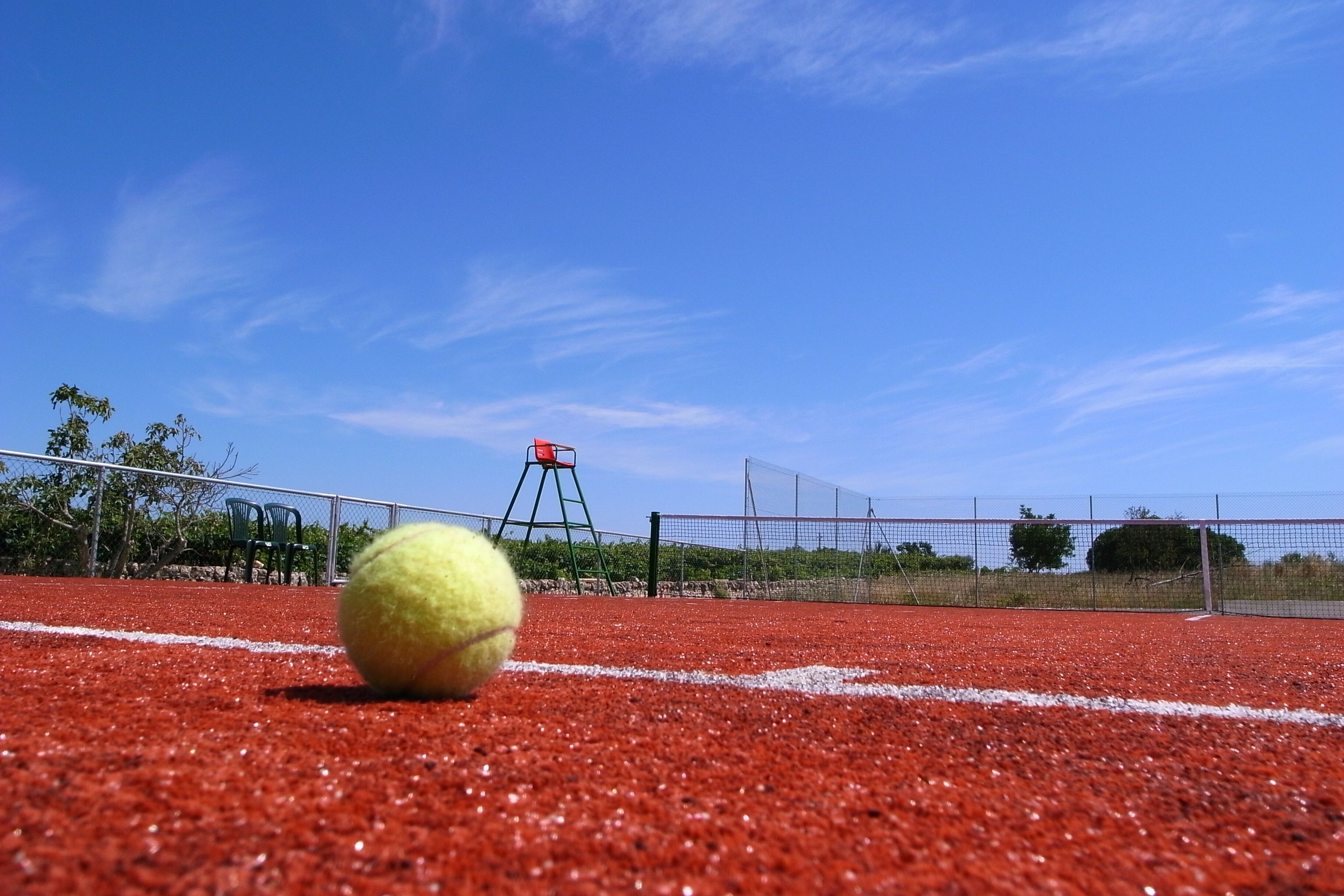 A tennis court with a yellow tennis ball in the foreground and a net in the background.