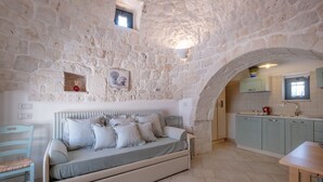 Quarto aconchegante com parede de pedra, uma cama, uma cadeira e um espaço para cozinha.