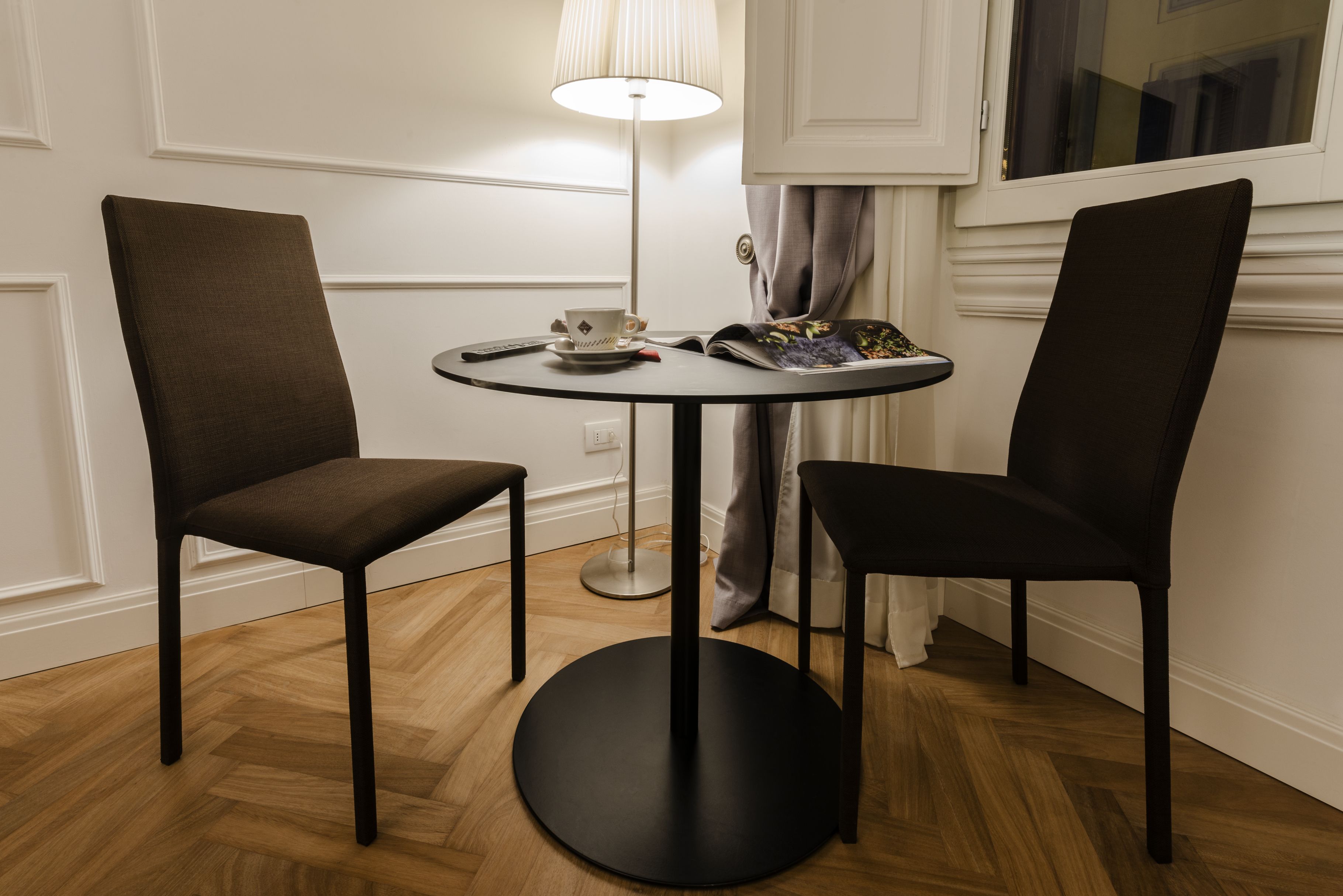Een kleine ronde tafel met twee stoelen, een lamp en een tijdschrift.