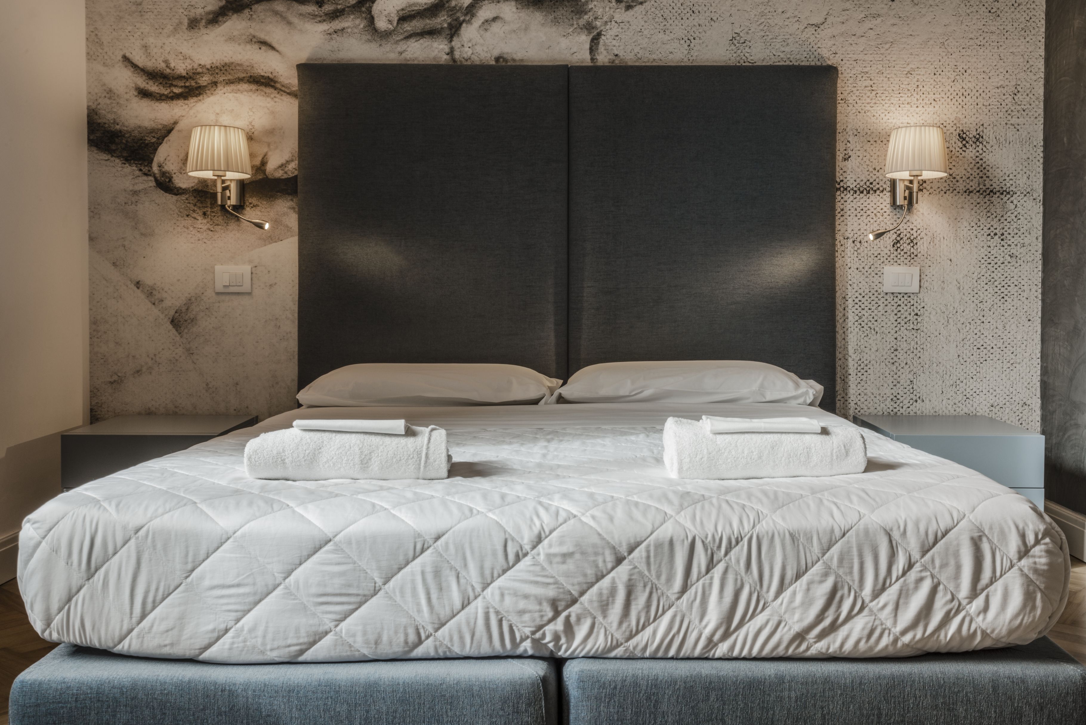 A modern bedroom with a large bed, two bedside lamps, and a textured wall.