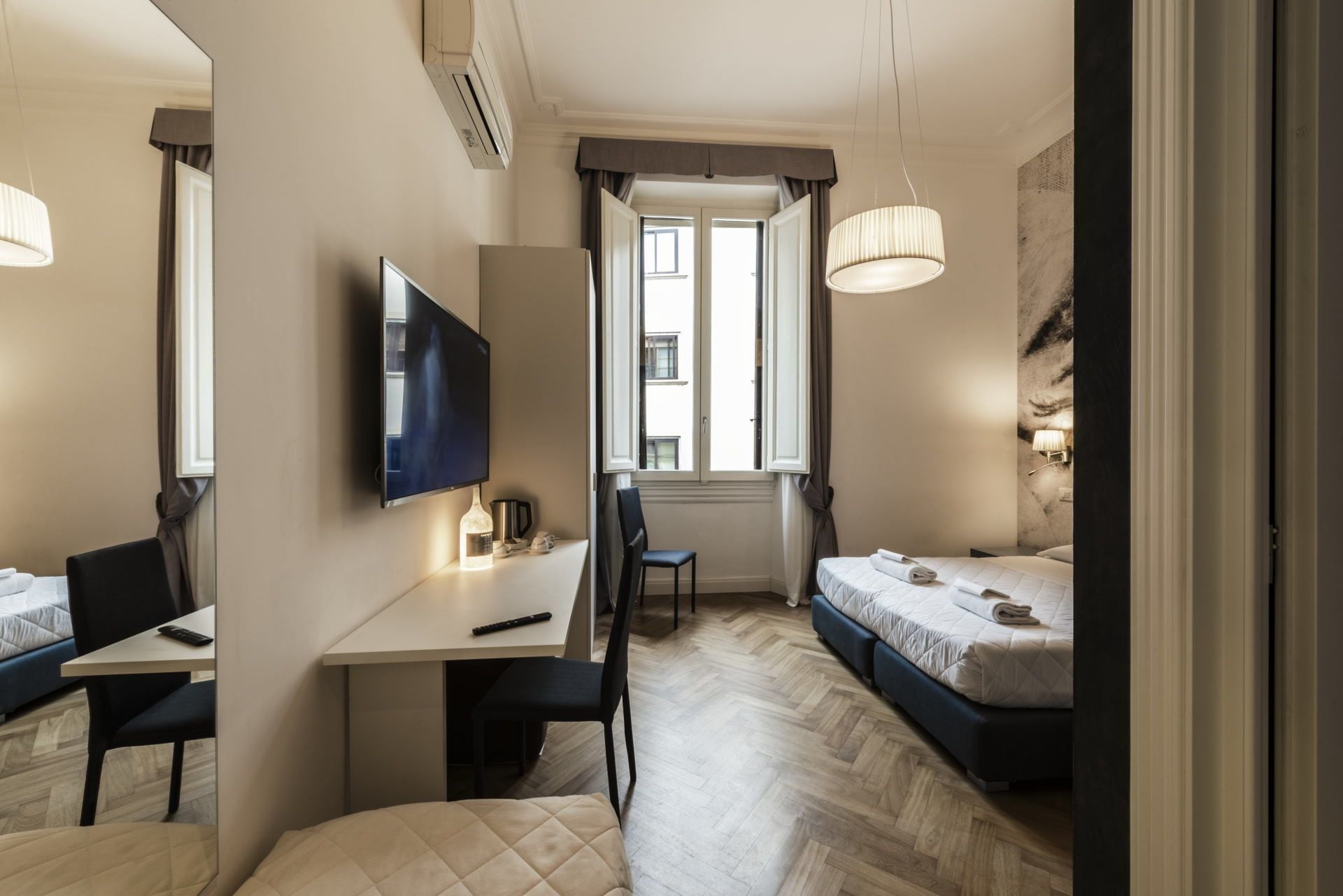 A modern hotel room with a bed, a desk, a chair, a TV, and a window with curtains.