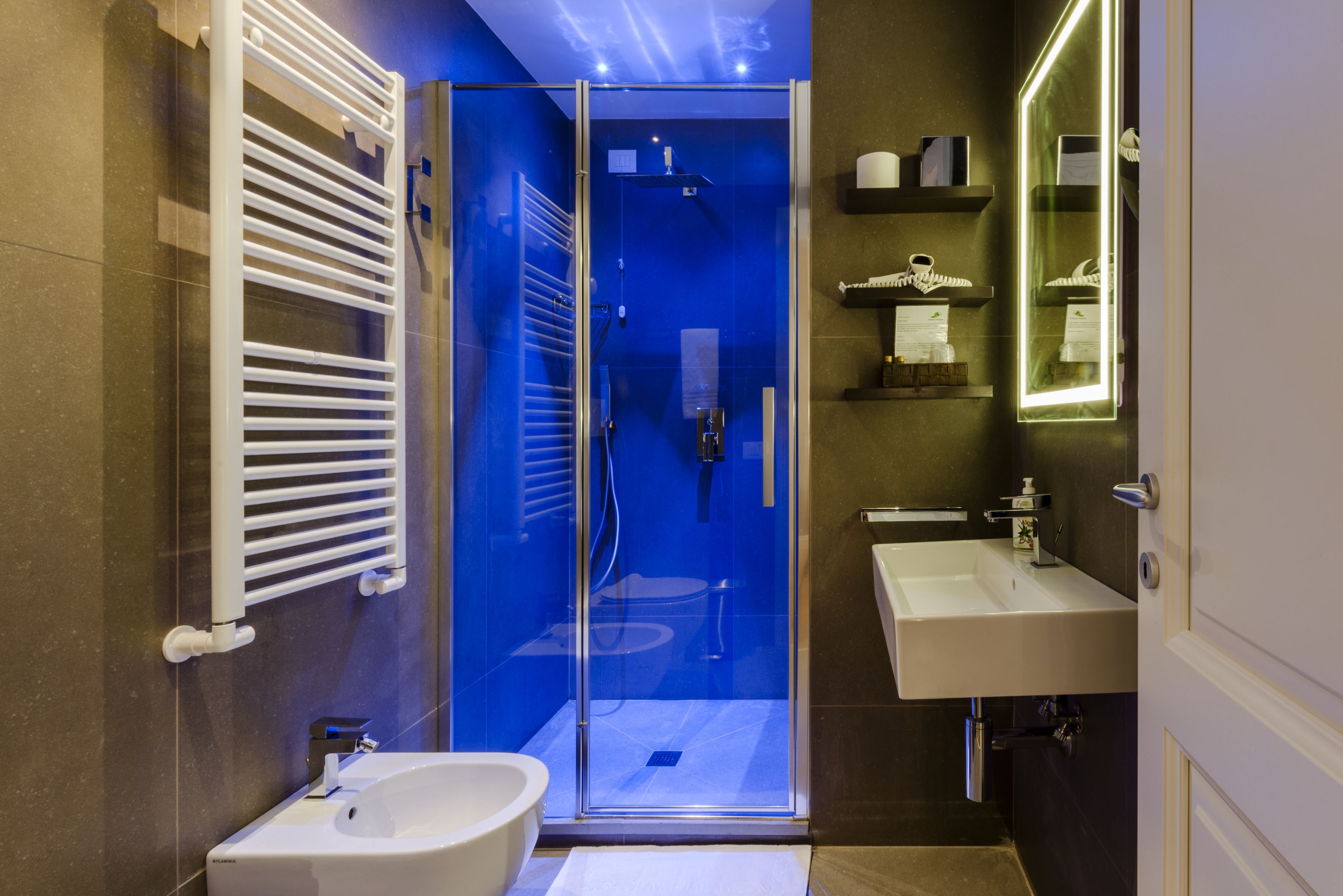 Un baño moderno con ducha envuelta en vidrio, un lavabo blanco y un espejo con repisas superiores.