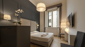 Habitación de hotel moderna con una cama, un escritorio y una silla. Cuenta con una ventana con cortinas, una planta en el escritorio y un televisor montado en la pared.
