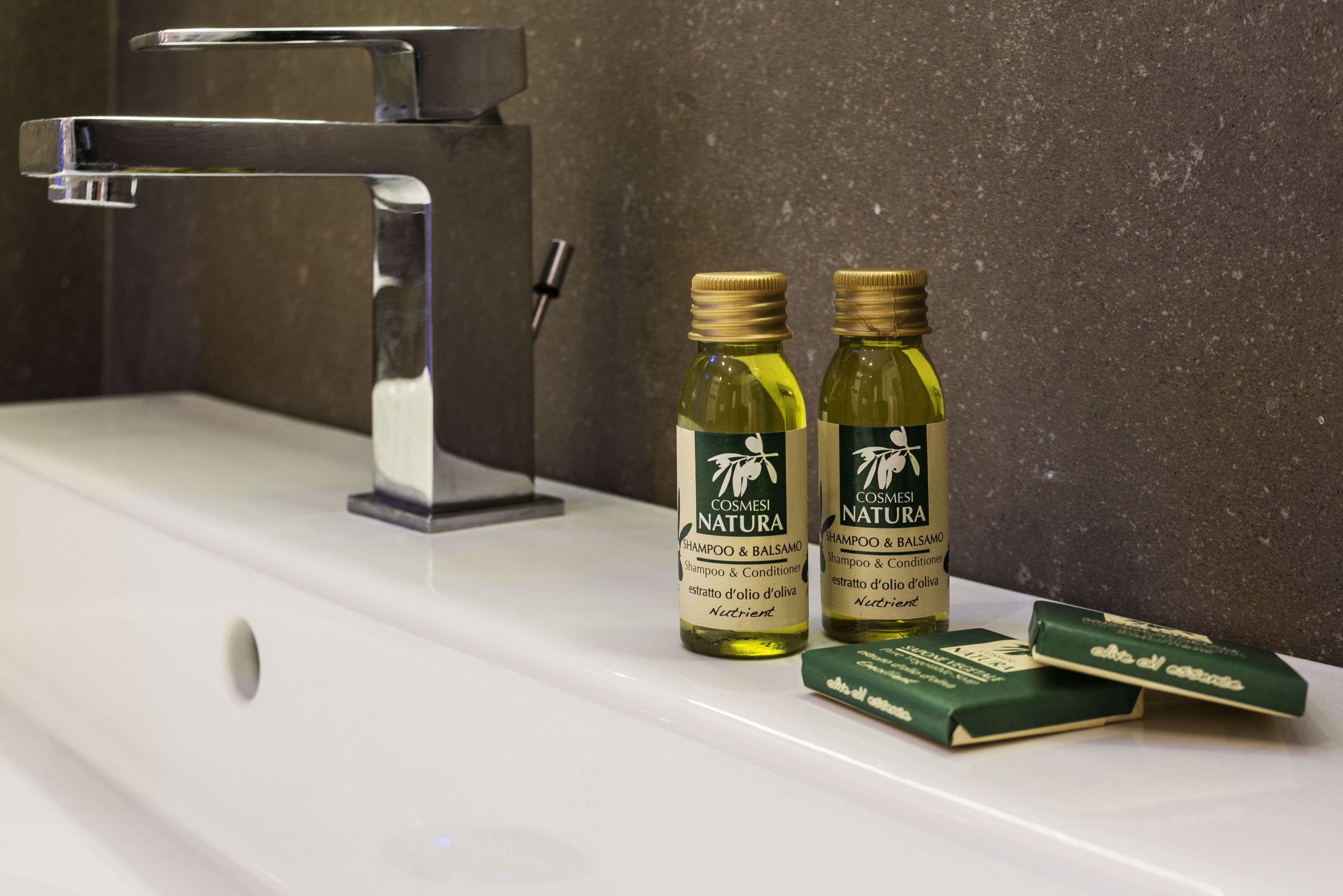 Ein Waschbecken mit zwei Flaschen Cosmesi Natura Shampoo und zwei grünen Seifenstücken.