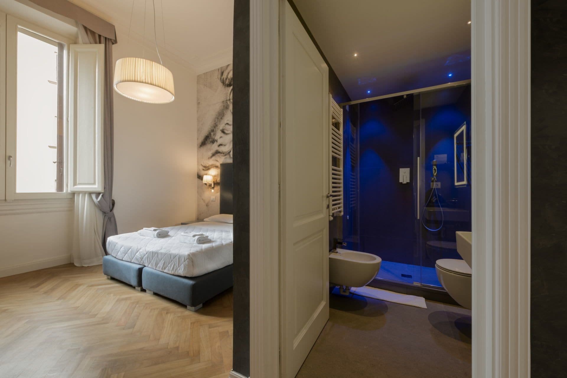 Un dormitorio con cama, mesita de noche y ventana. Cuenta con un baño con inodoro, lavabo y ducha.