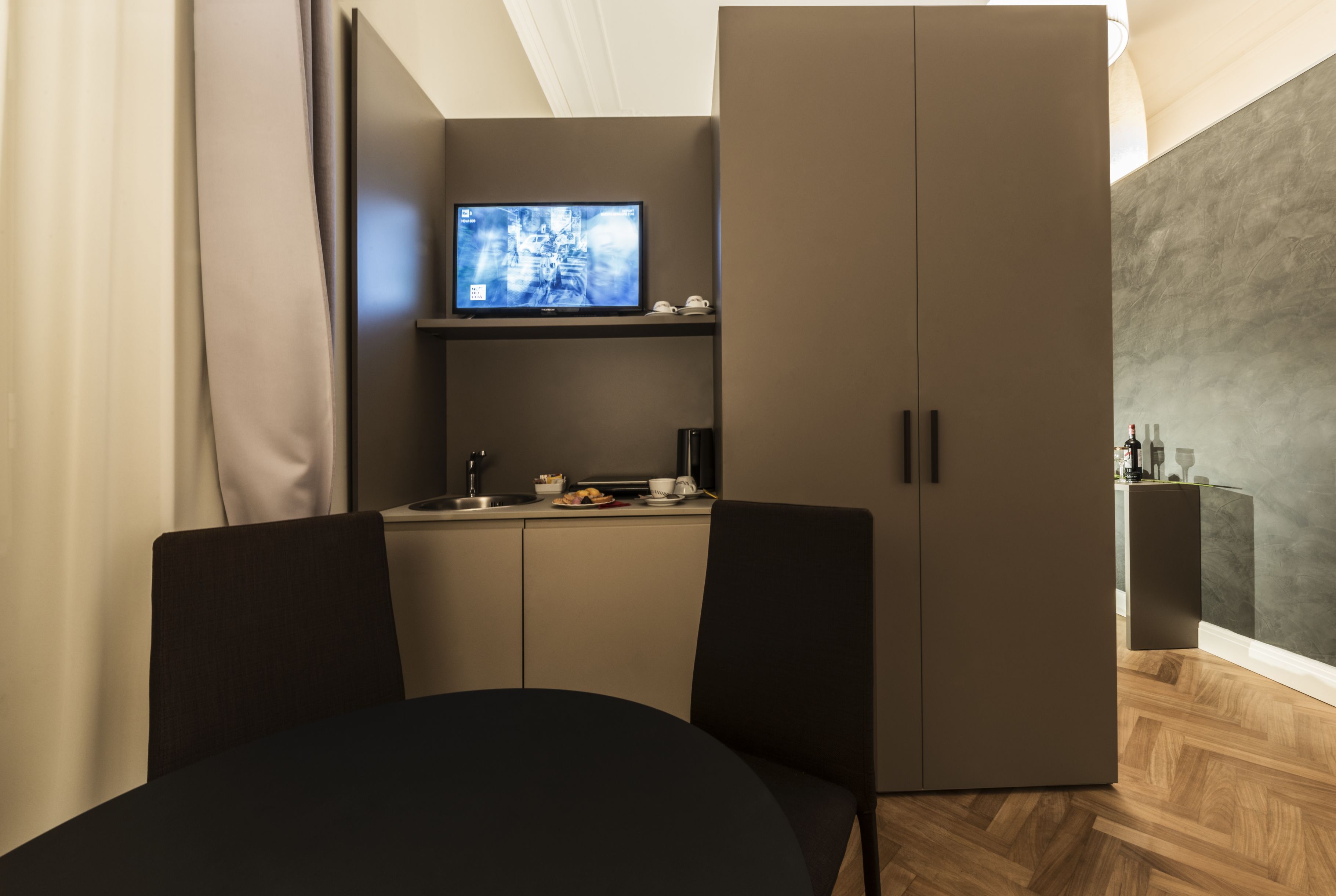 Une chambre moderne avec une table à manger, deux chaises, un téléviseur posé sur une étagère et une armoire.