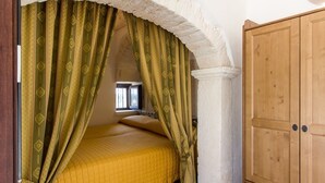 Een slaapkamer met een bed onder een rondbogig raam, een houten garderobe en groene gordijnen.