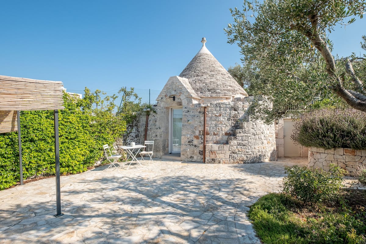 Un bâtiment en pierre doté d’un toit conique, d’une porte et d’un petit patio avec une table et des chaises.