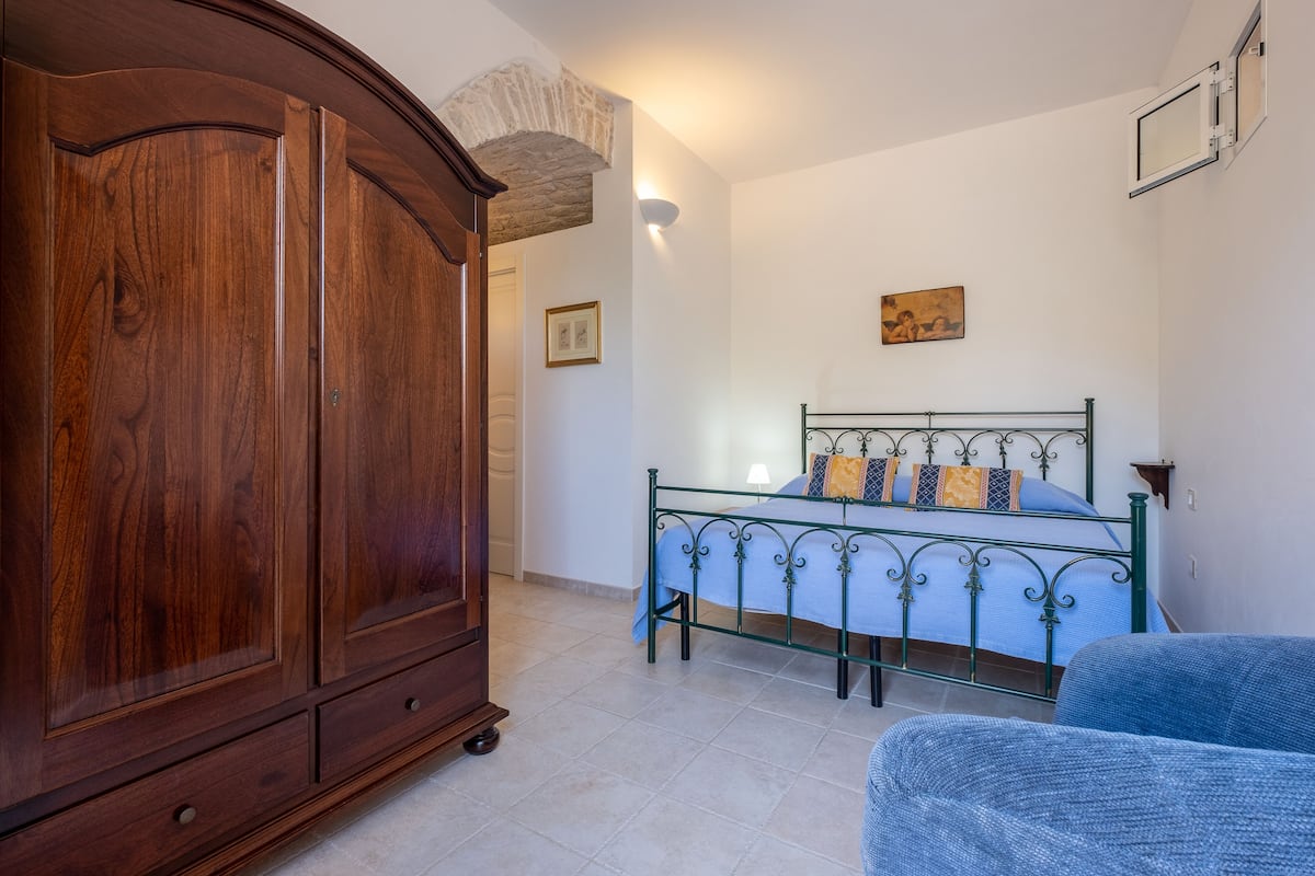 Une chambre avec une armoire en bois, un cadre de lit en métal et une chaise bleue.