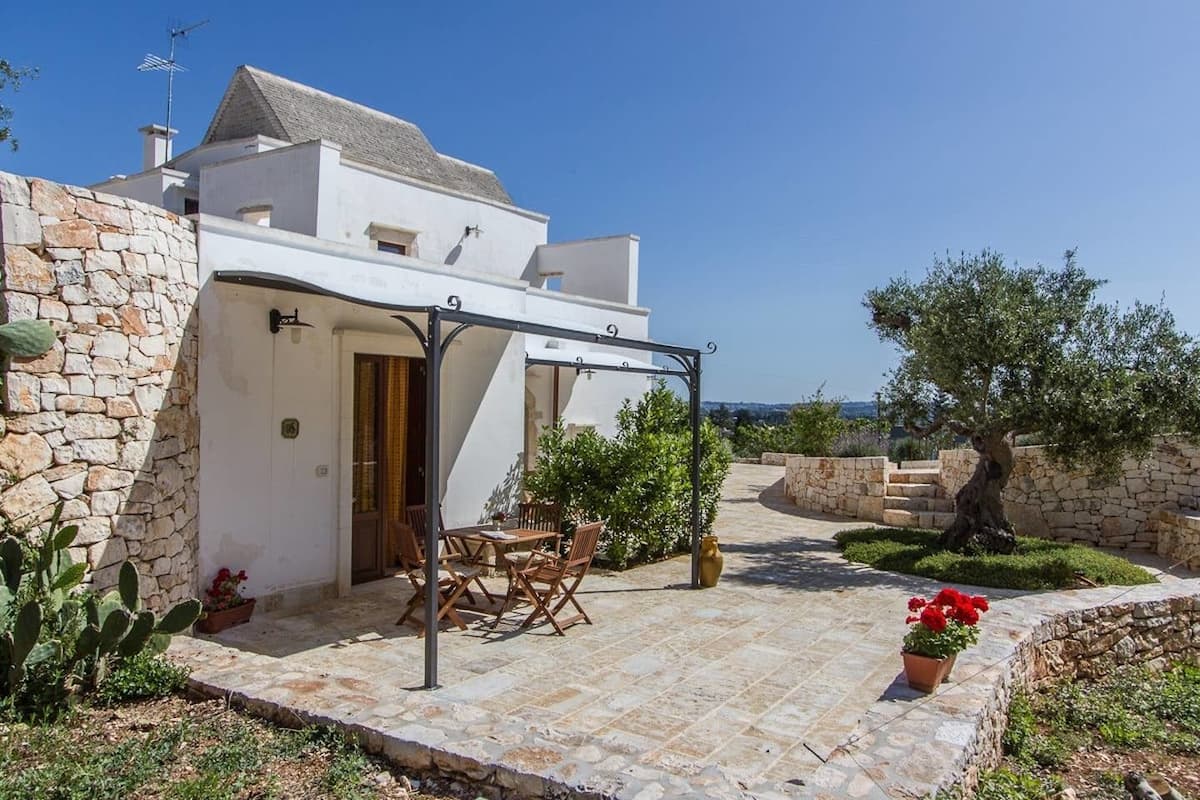 Un bâtiment blanc à l’extérieur en pierre, une terrasse couverte avec des meubles en bois et une vue sur la mer.