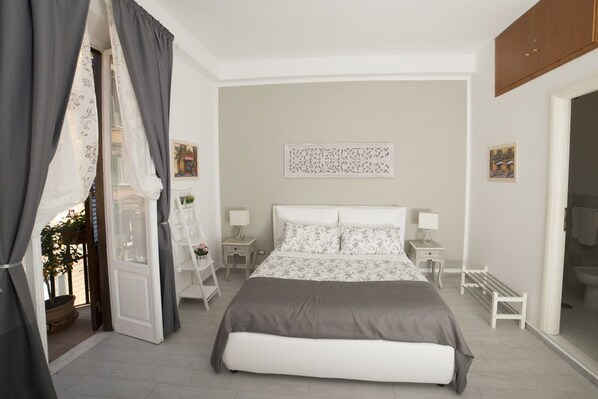 Un dormitorio con una cama grande, mesitas de noche, un armario y una puerta con cortinas.