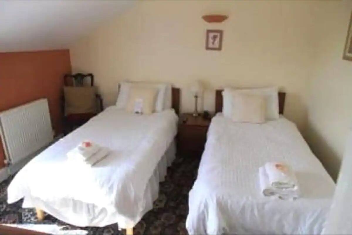 A hotel room with two single beds, a small table, and a chair.