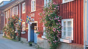 A red building with a café sign, Swedish flags, and pink flowers. - Garvaregården Hotel and B&B (Askersund)