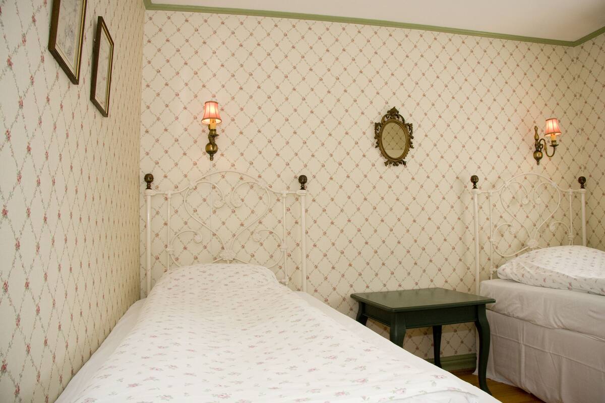 Une chambre avec deux lits, une petite table et des lampes fixées au mur.