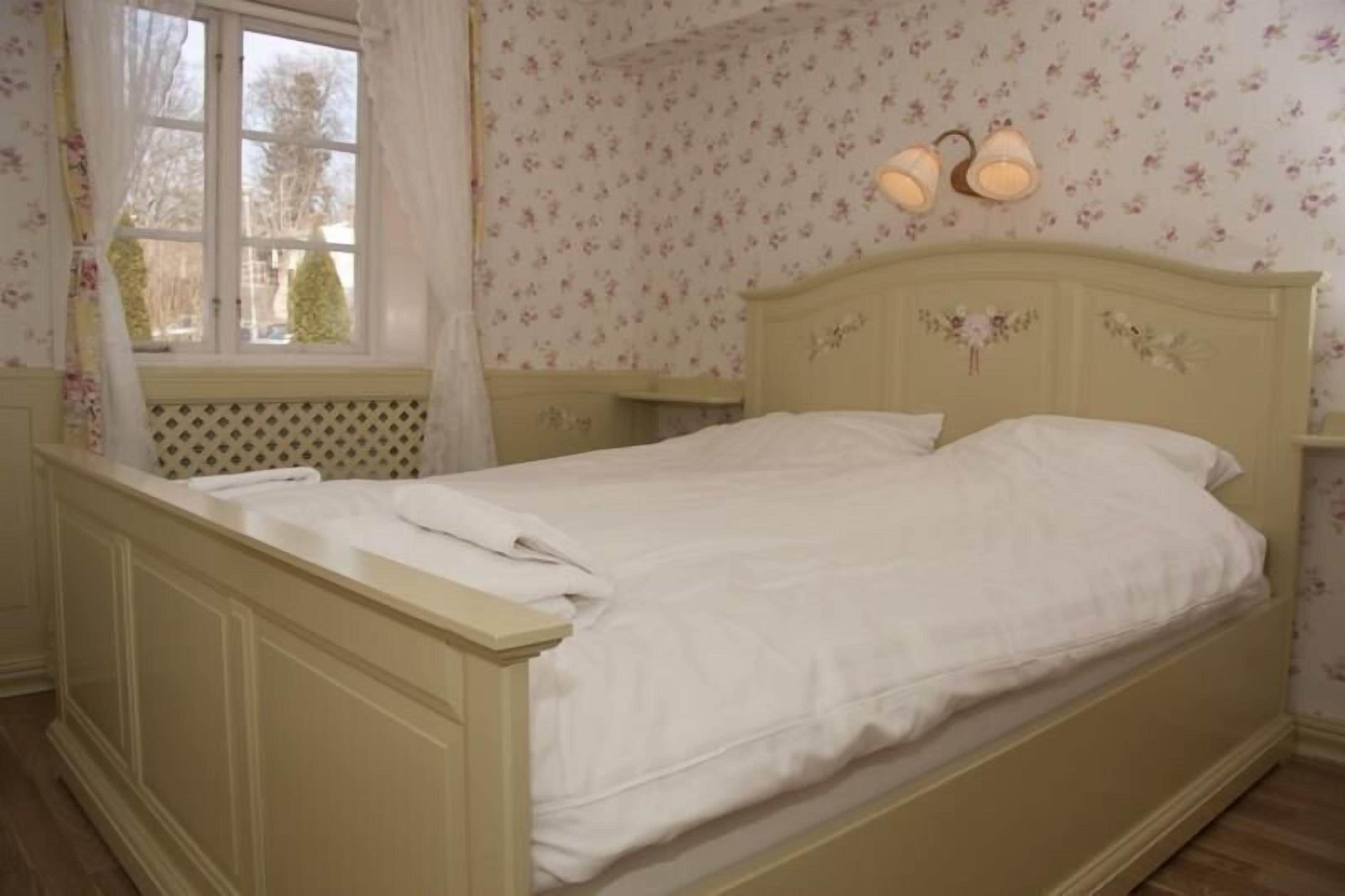 A bed with a headboard, a window with curtains, and floral wallpaper.