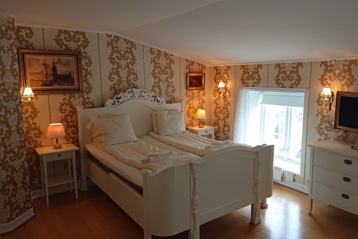 Une chambre à coucher avec un lit blanc, deux tables de chevet avec des lampes, une commode et un téléviseur posé sur un meuble.