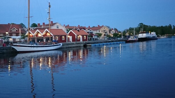 A calm waterfront with a white boat docked near buildings with red roofs. - Garvaregården Hotel and B&B (Askersund)