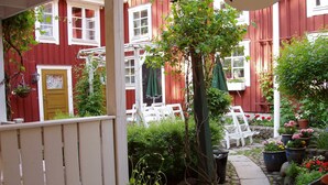 A red building with white windows and a yellow door, surrounded by greenery and outdoor seating. - Garvaregården Hotel and B&B (Askersund)