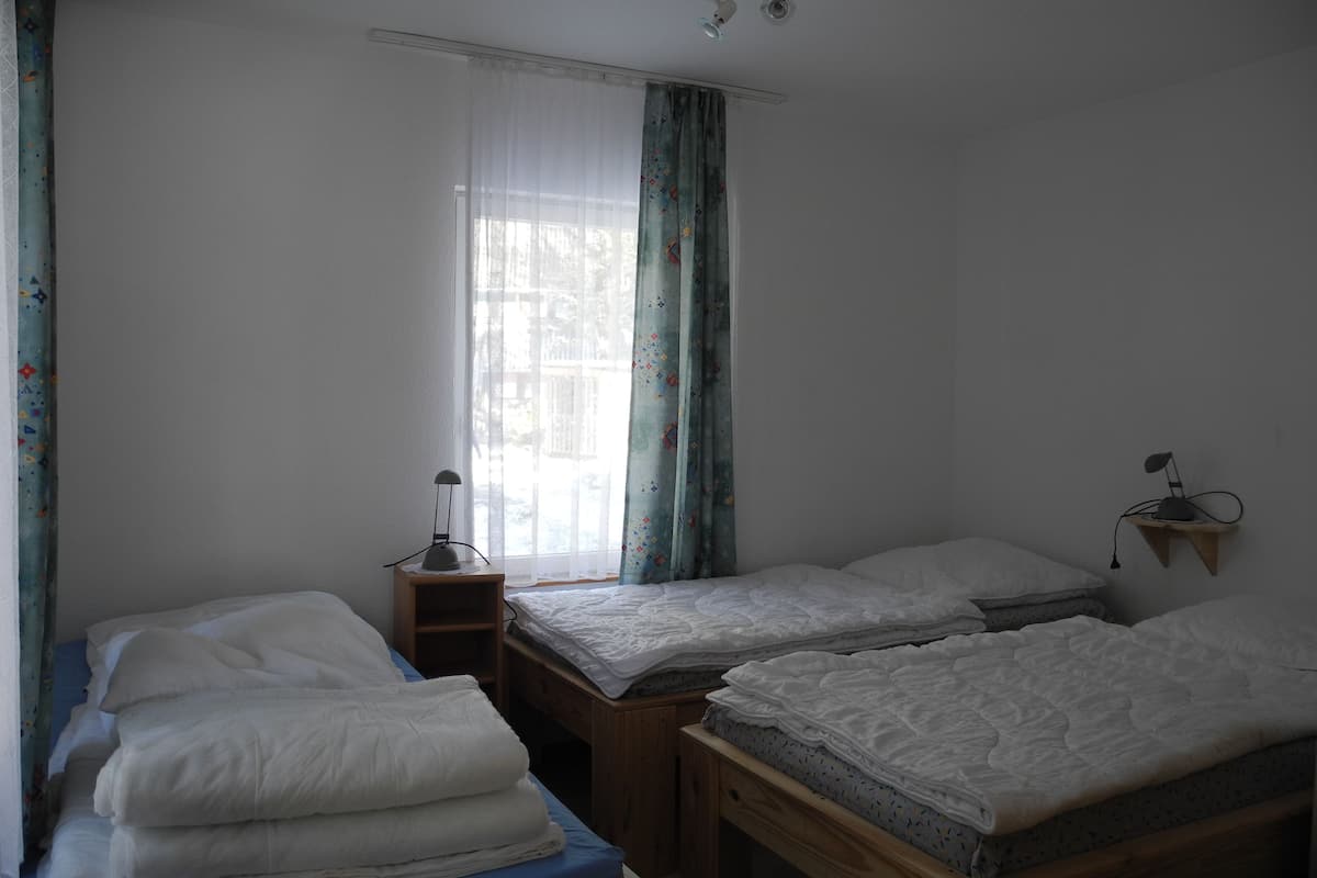 A room with three beds, a nightstand with a lamp, and a window with curtains.