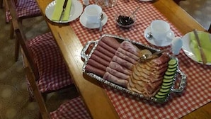 Una escena de desayuno con una mesa larga, manteles a cuadros y diversas opciones para el desayuno, incluyendo pasteles, ponche de frutas y una bandeja con jamón y pepino.