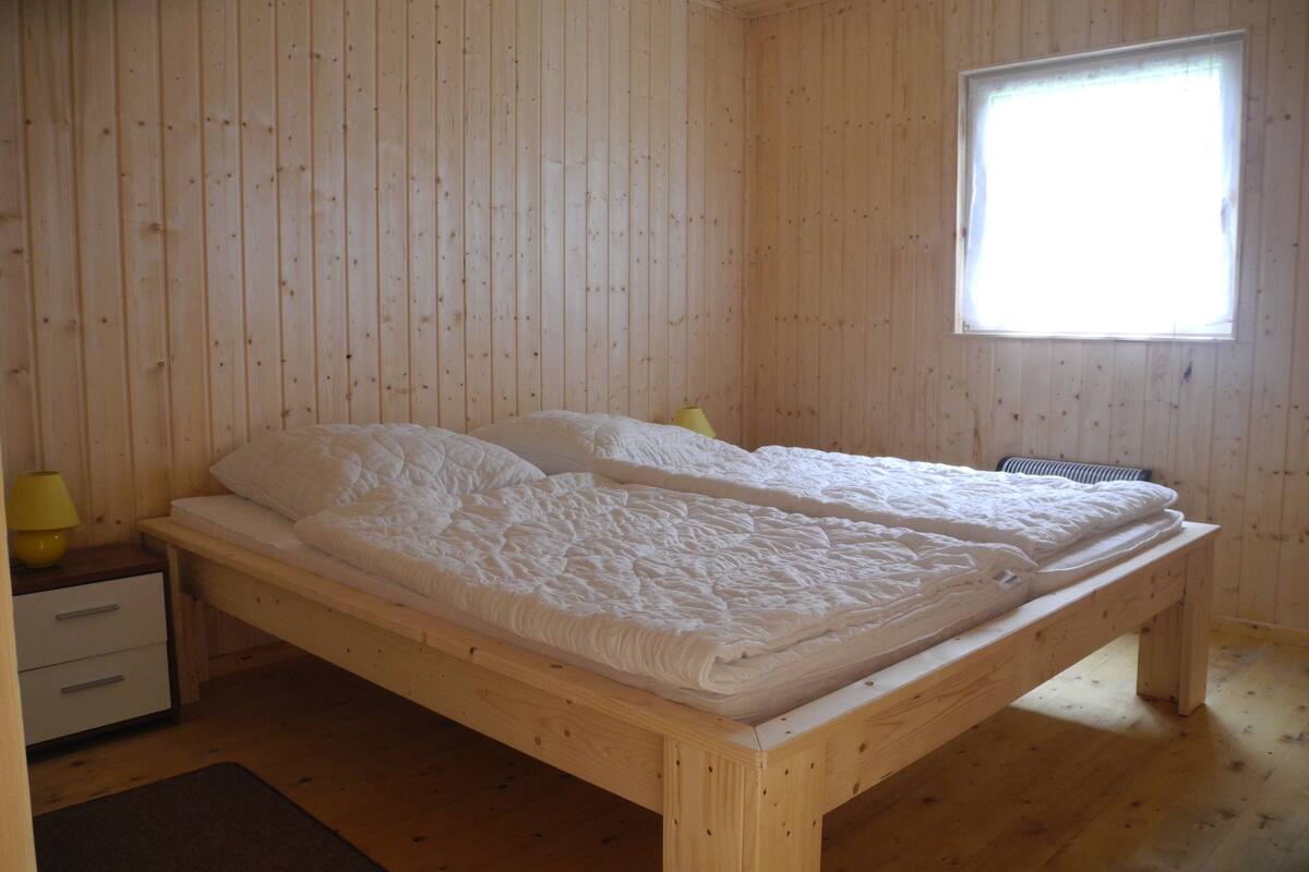 A wooden-paneled room with a bed, a nightstand, and a window.