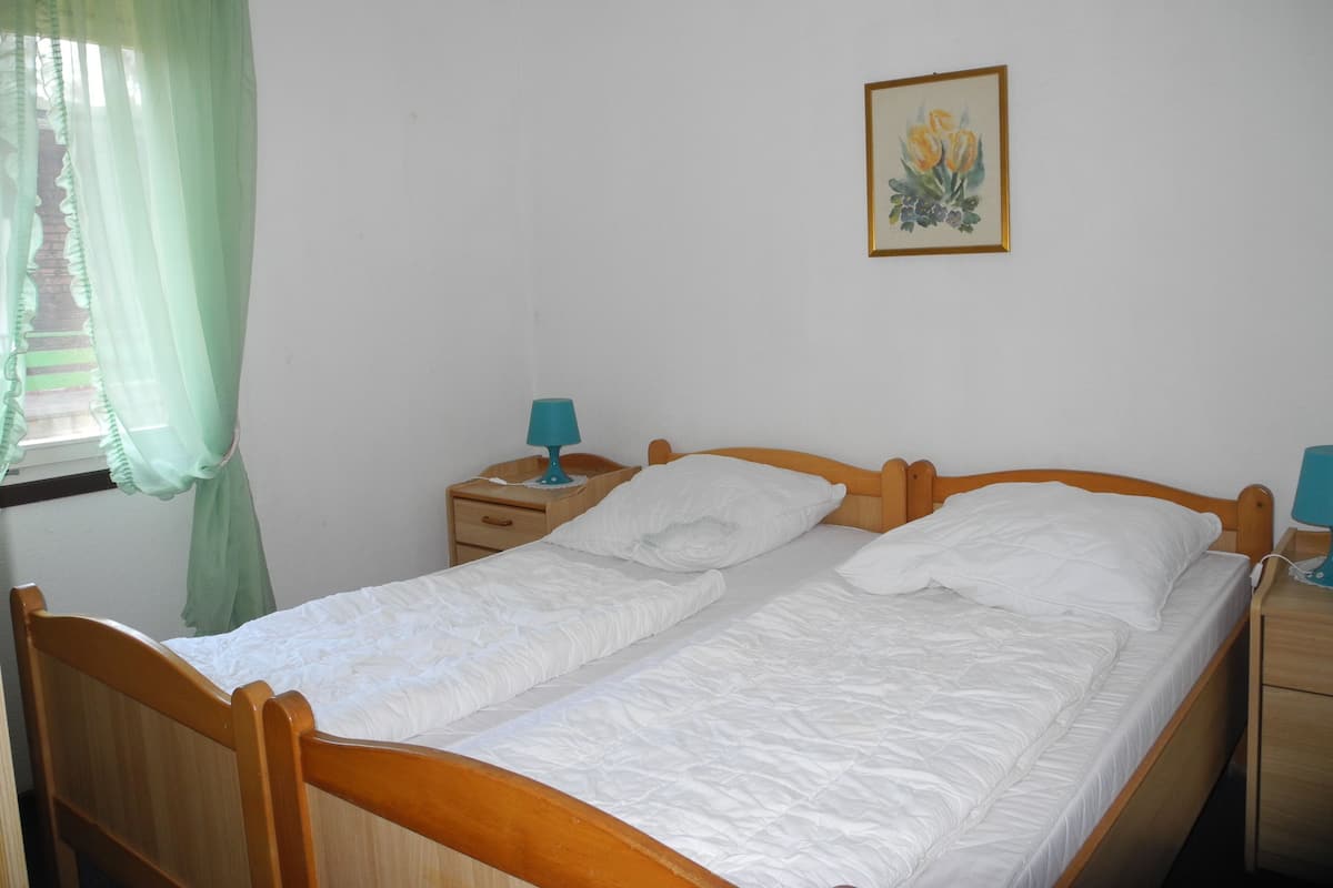 A double bed with a wooden frame, a nightstand with a lamp, and a painting on the wall.