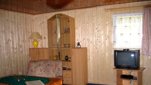 Una habitación acogedora con detalles de madera, un televisor sobre un mueble, una mesa con una lámpara y una silla.