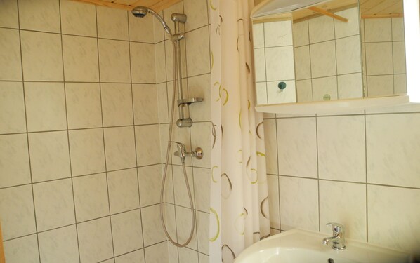 Un baño con ducha, lavabo y espejo.