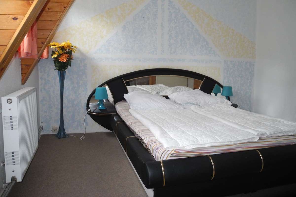 A bedroom with a bed, bedside lamps, a radiator, and a flower vase.