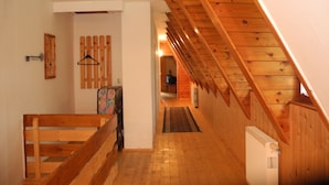Un pasillo estrecho con suelo de madera, un banco, un radiador y una escalera de madera.