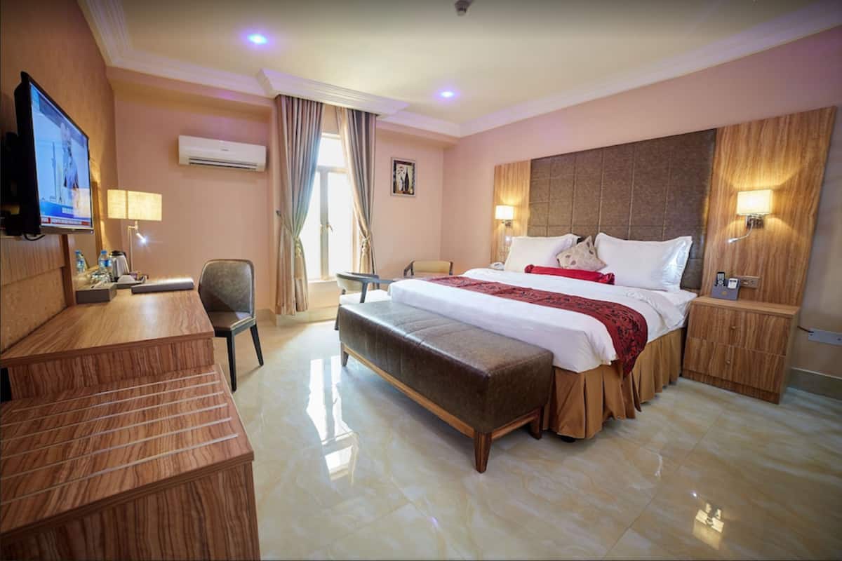 A hotel room with a large bed, a desk, a chair, a TV, and a wardrobe.