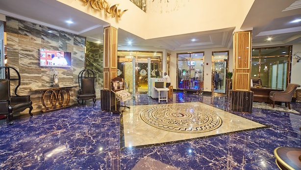 A lobby with a marble floor, a large decorative rug, and a television mounted on the wall. - Corinthia Villa Hotel (Abuja)