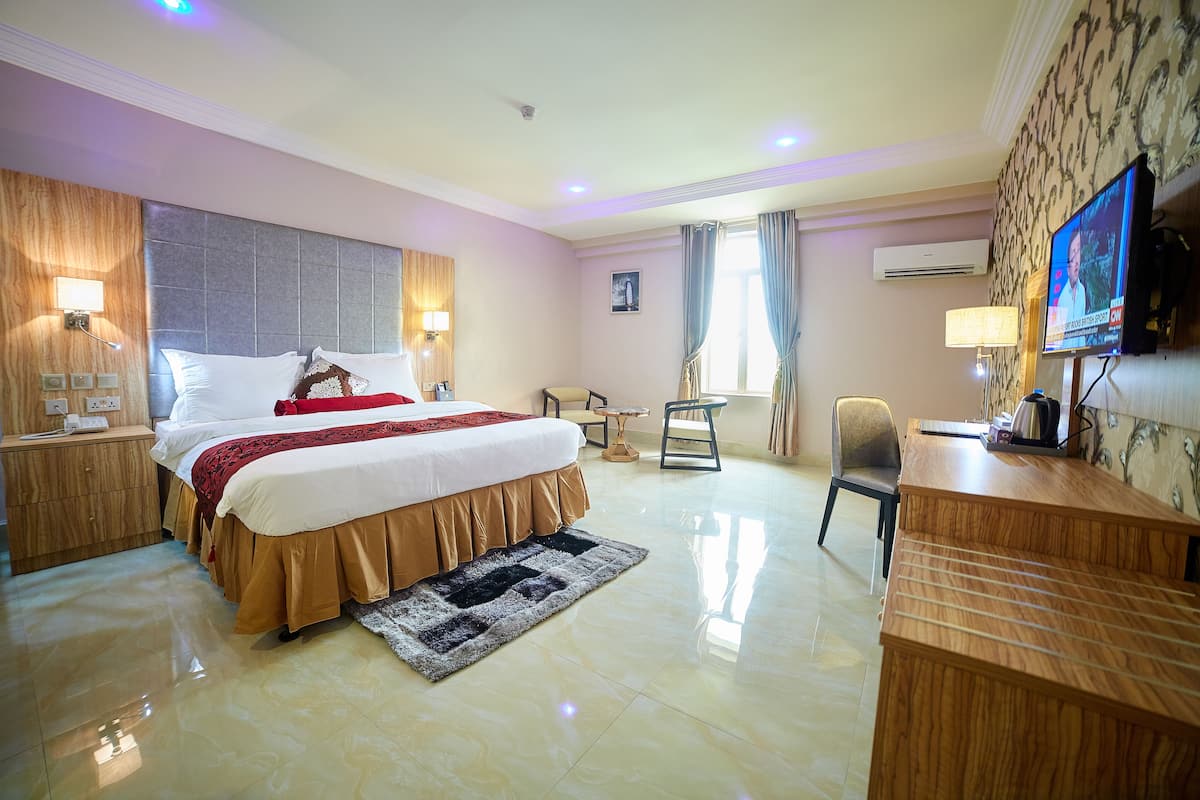 A hotel room with a large bed, a desk, a chair, and a television.