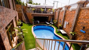 A swimming pool surrounded by brick walls, a covered patio, and a staircase leading to an upper level. - Corinthia Villa Hotel (Abuja)