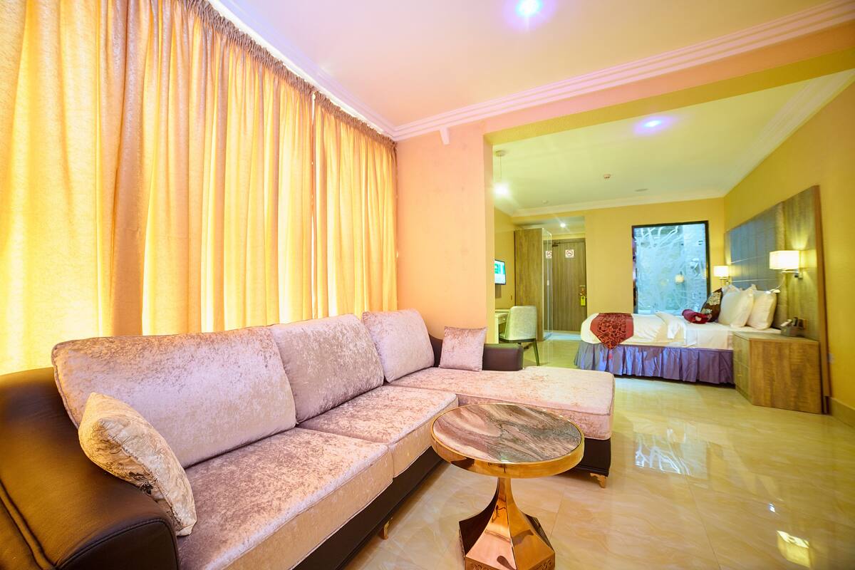 A hotel room with a sofa, a round coffee table, a bed with a headboard, and a nightstand.