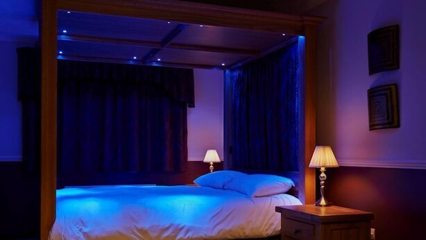 A four-poster bed with a canopy, two bedside lamps, and a wooden nightstand with drawers. - Hillview Park (Beauly)