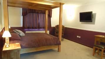 A four-poster bed with a wooden frame and a headboard, a bedside table with a lamp, a chair, and a television mounted on the wall.
