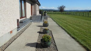 A building with a concrete exterior, a paved pathway, and potted plants. - Hillview Park (Beauly)