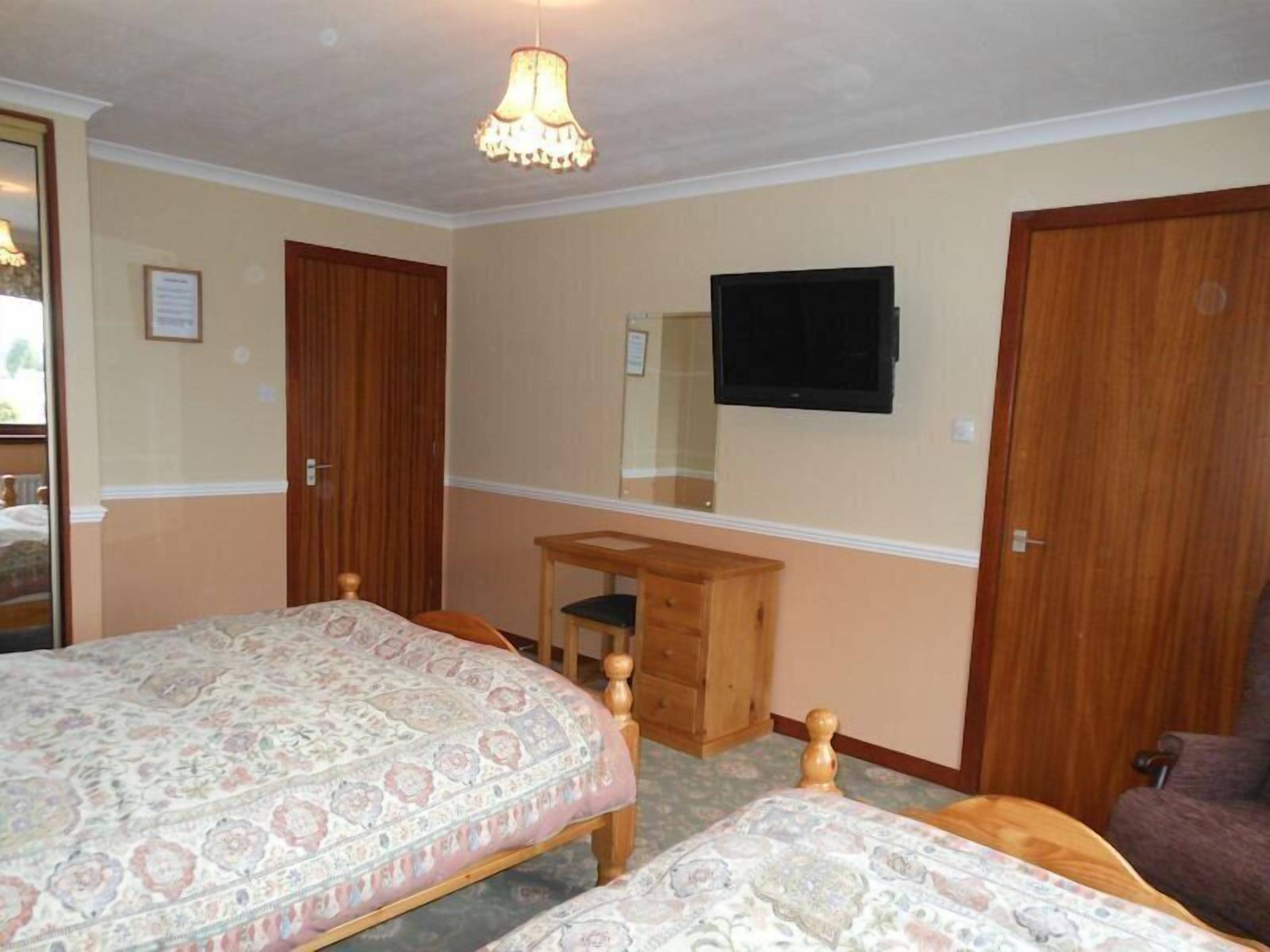 A bedroom with two beds, a wooden desk, a chair, a television, and a wardrobe.