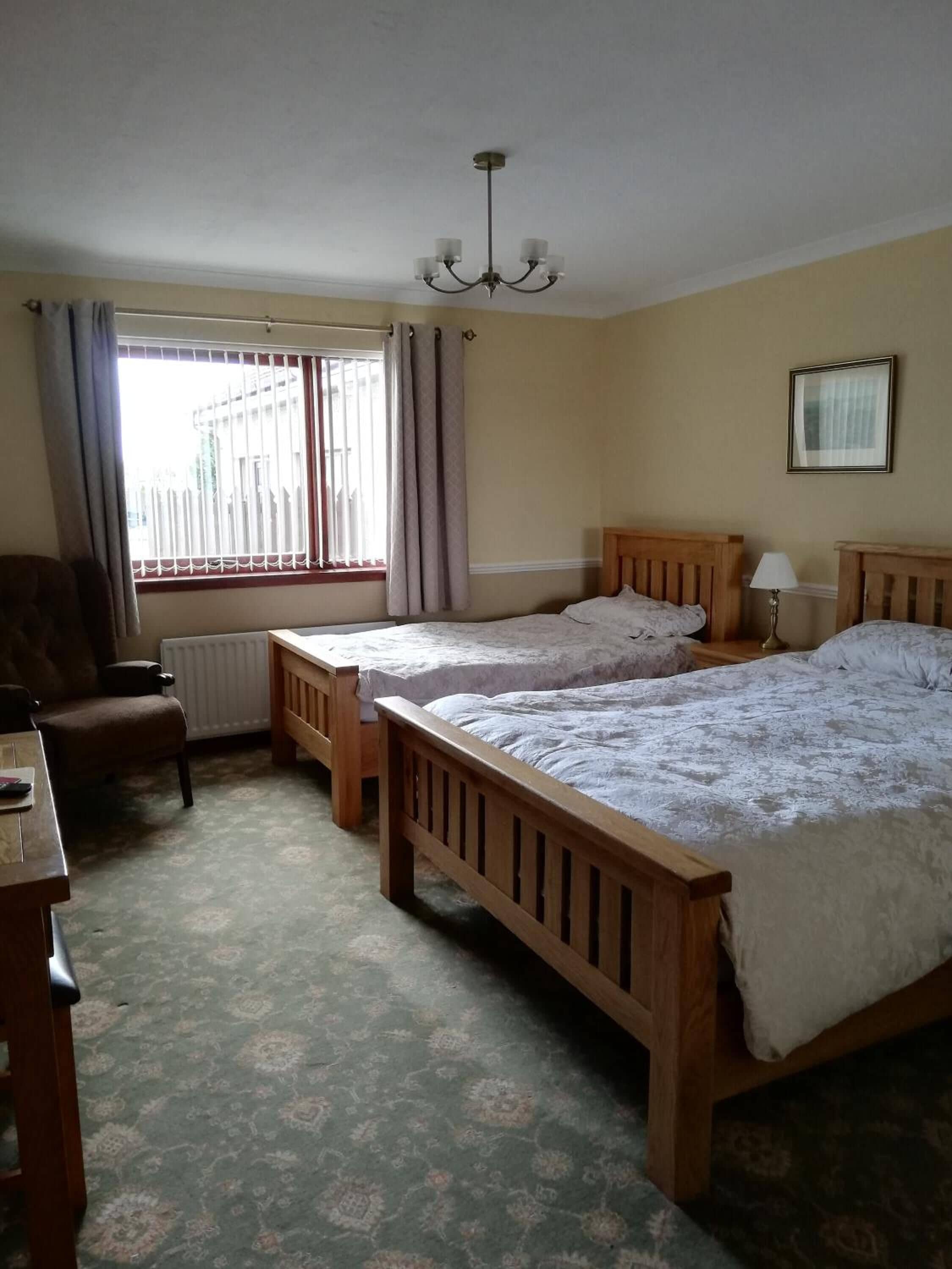 Een hotelkamer met twee houten bedden, een stoel, een tafel, een radiator en een raam met gordijnen.