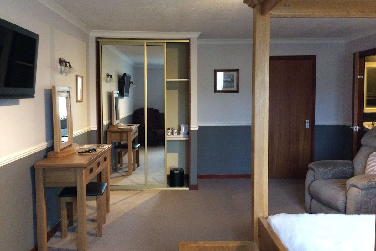 A hotel room with a bed, a desk, a chair, a wardrobe, and a television.