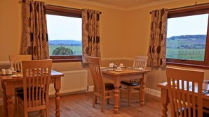 A dining area with a table and four chairs, large windows with curtains, and a view of the countryside. - Hillview Park (Beauly)