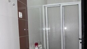 Un baño con un lavamanos blanco, un tapete de baño rojo y negro, y una zona de ducha con puertas de vidrio esmerilado.