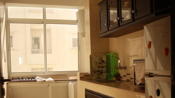 Una cocina con ventana, armarios, un refrigerador y una alfombra estampada.