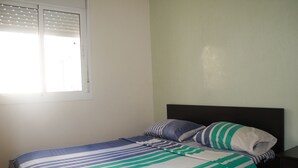 Una cama con ropa de cama a rayas, una mesita de noche y una ventana con persianas.