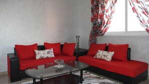 Una sala de estar con un sofá rojo, una mesa de centro de vidrio y una alfombra estampada.
