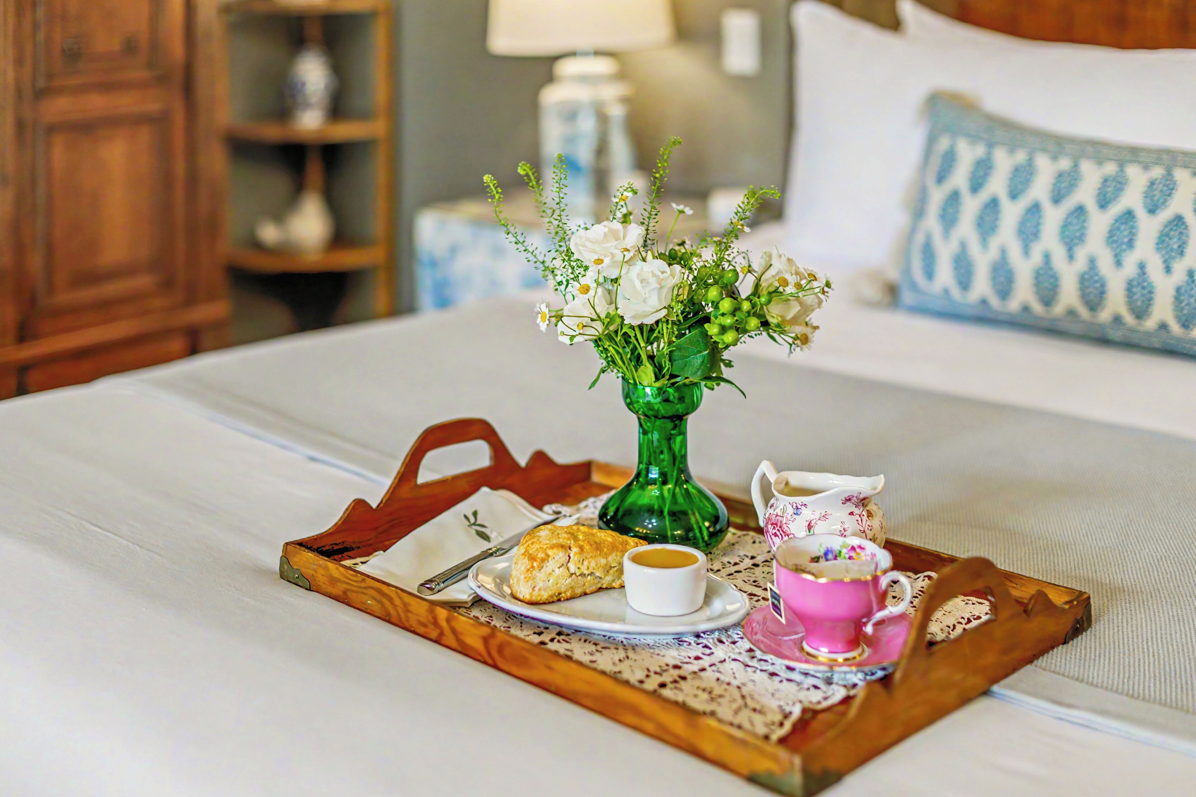 A tray with a pastry, a cup of coffee, and a teapot on a bed.