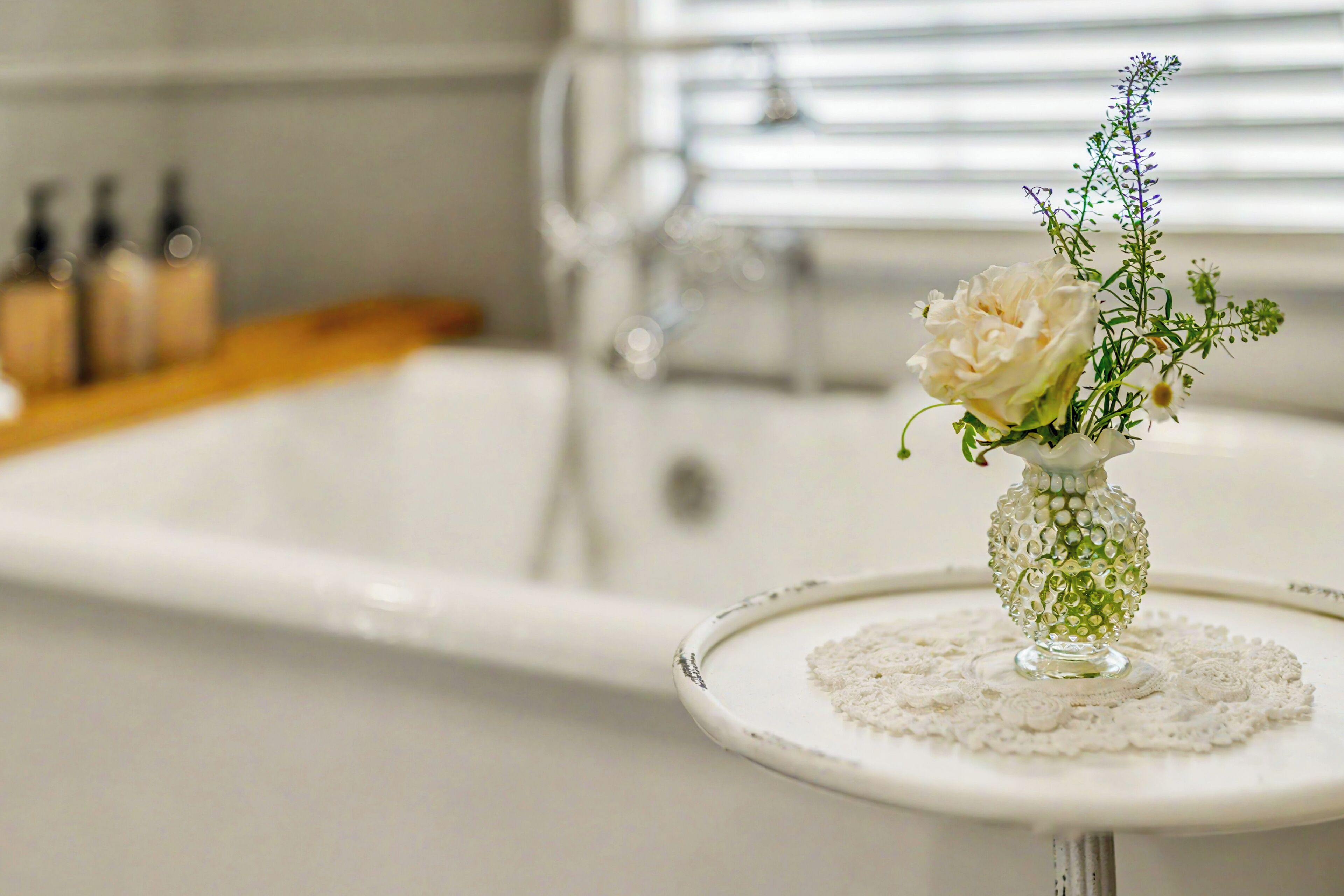 Een badkamer met een wit wastafel, een glazen vaas met bloemen en een flesje lotion op het aanrecht.