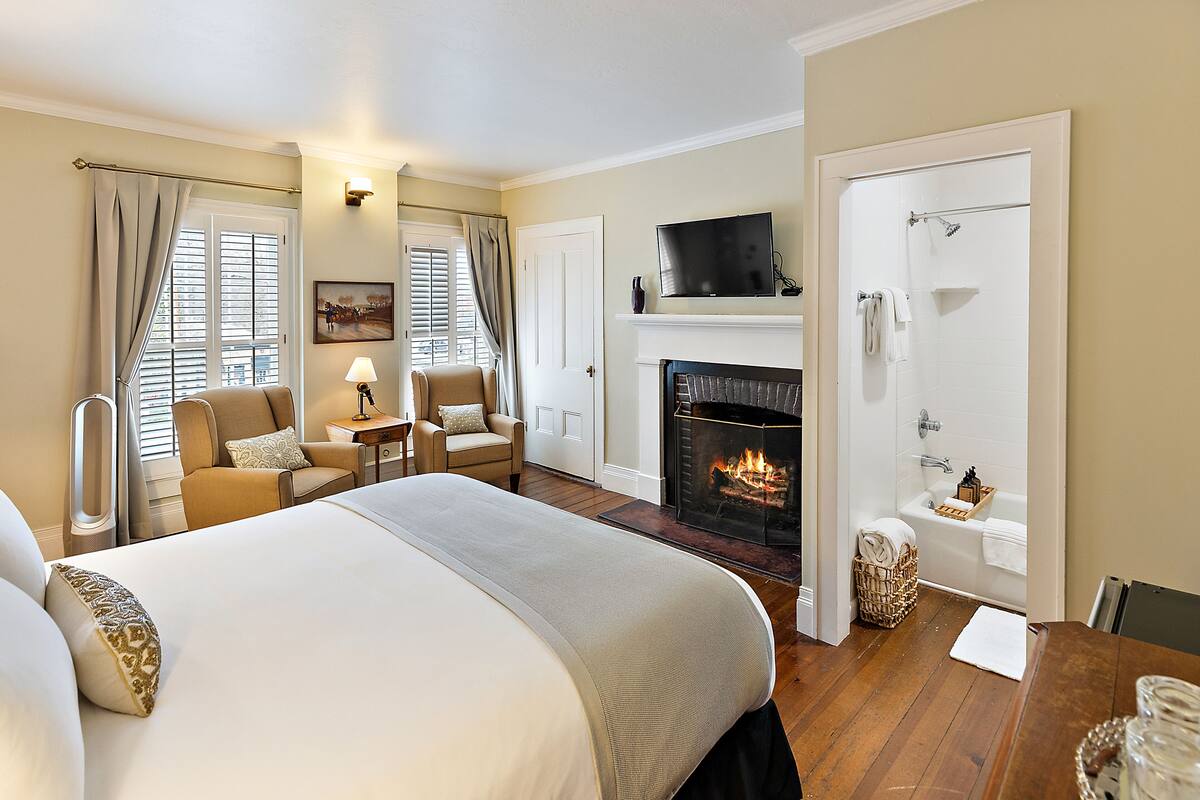 A hotel room with a large bed, a fireplace, a television, and a bathroom with a shower and bathtub.